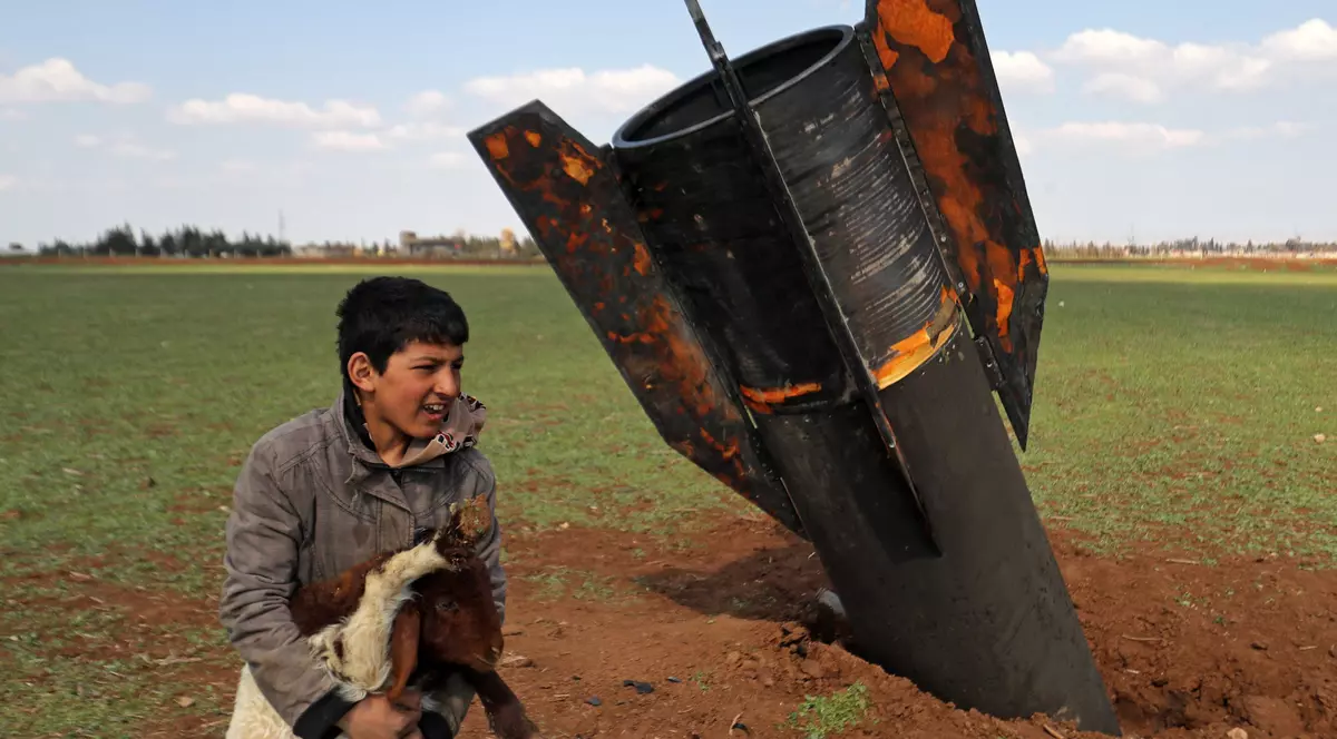 Un copil se joacă lângă o racheta neexplodată aterizată pe un câmp din Siria. Băiatul era cu oile la păscut.