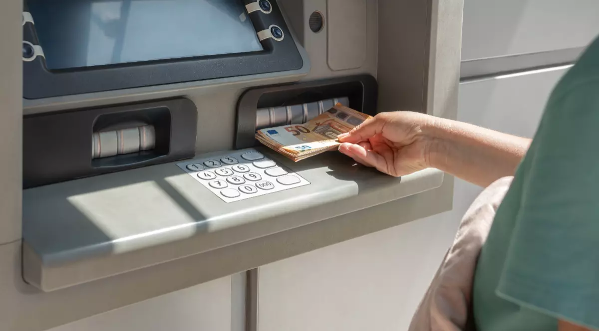 Un bărbat în tricou, în timp ce scoate bani cash, hârstii de 50 de euro din bancomat