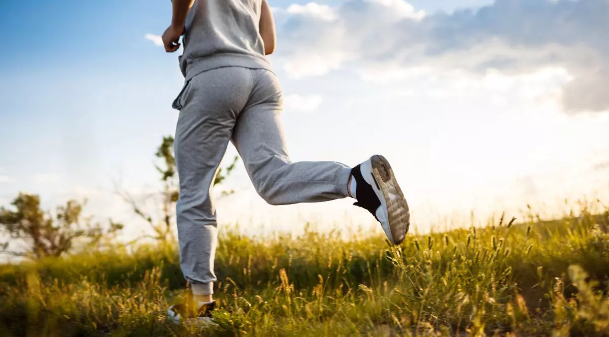 Prim-plan cu un bărbat sportiv care aleargă pe câmp la răsărit.