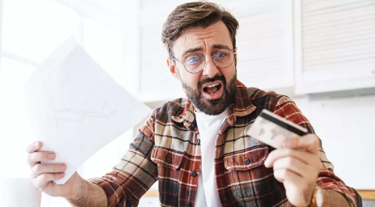 Portretul unui bărba șocat care ține un card de credit în mână și o hartie în cealaltă mână