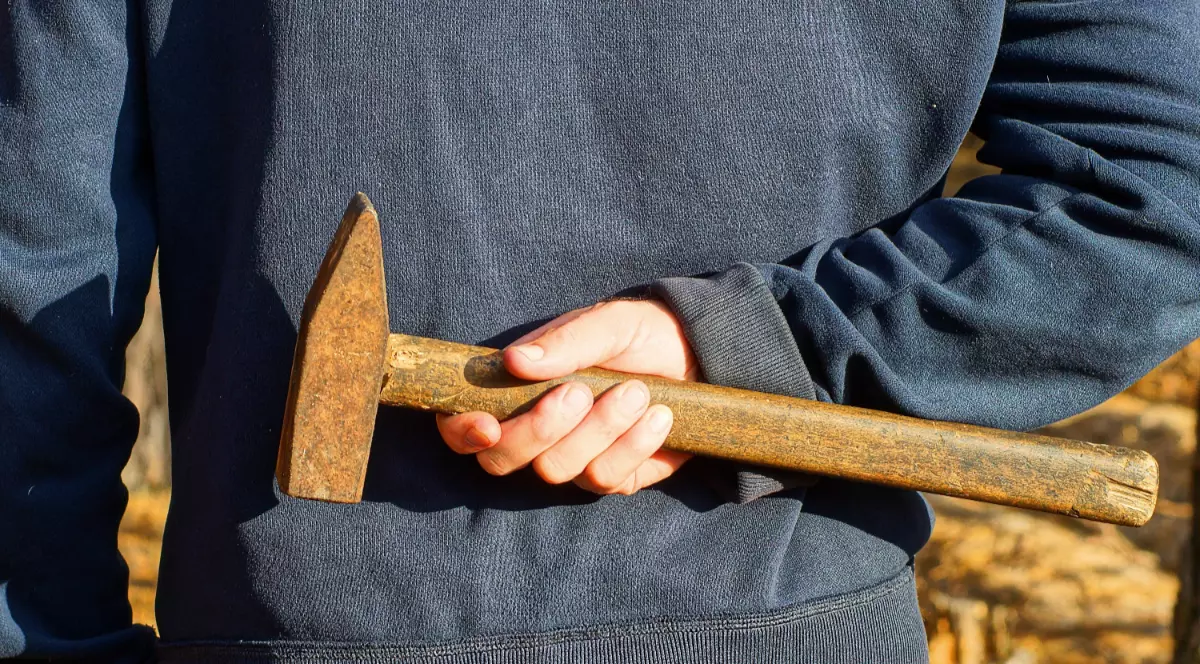 Un bărbat în pulover care ține la spate un ciocan.