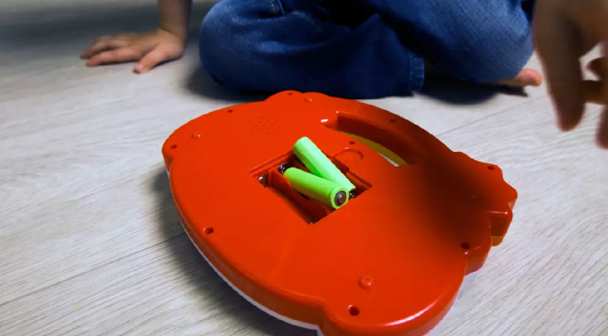 Baterii verzi într-o juărie roșie de plastic, lângă care stă un copil