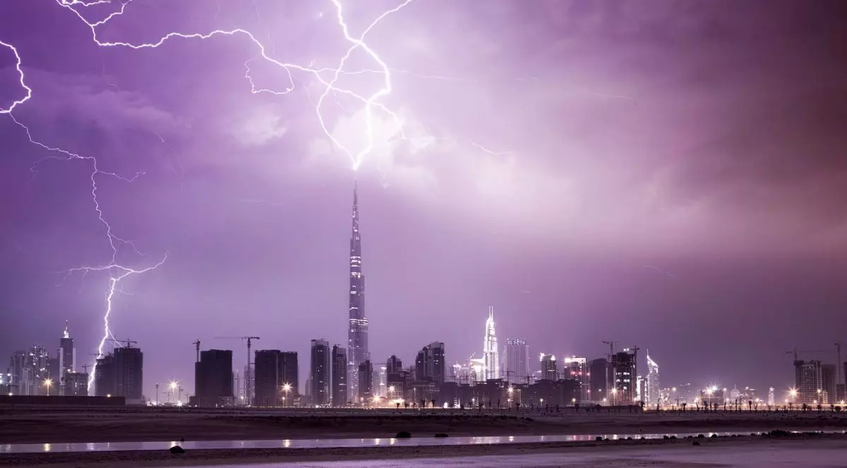 panoramă nocturnă a dubaiului cu zgârie-nori, dominată de o nuanță intensă de violet și mov care colorează cerul încărcat de nori. În centrul compoziției se află hotelul Burj Khalifa, al cărei vârf pare să atingă originea unor descărcări electrice ramificate și luminoase care brăzdează partea superioară a imaginii, Dubai, noiembrie 2013
