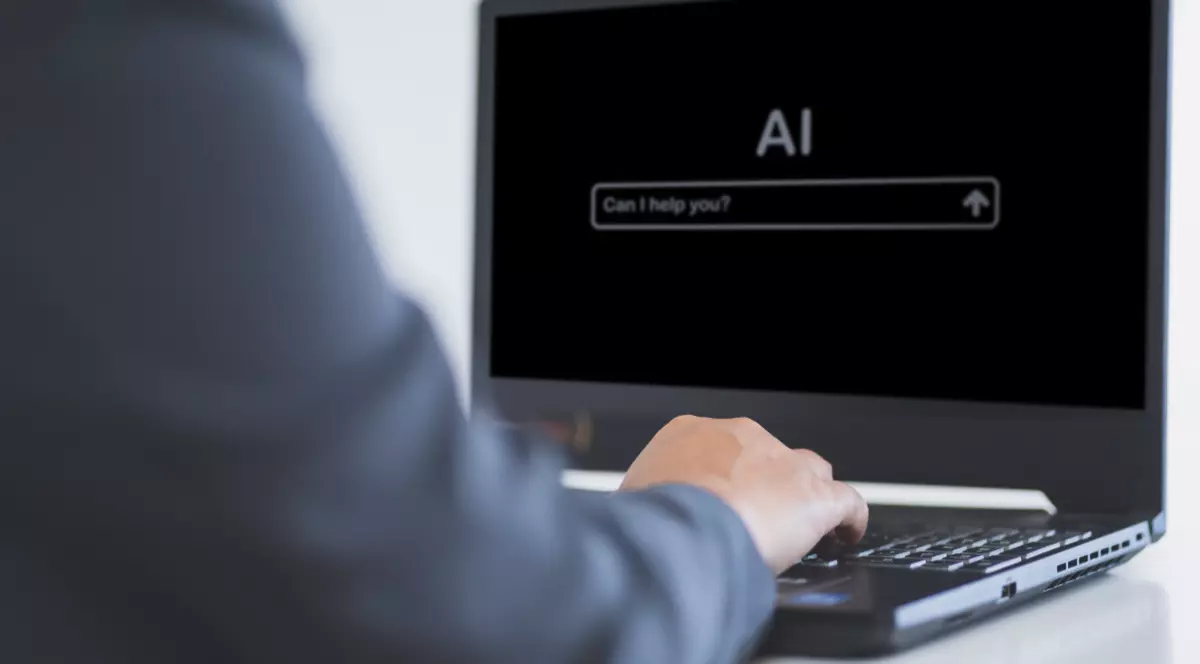 Un bărbat care scrie pe un laptop pe ecranul căruia scrie AI