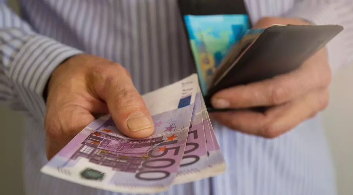 Un bărbat ține într-o mână patru bancnote de 500 de euro, iar în cealaltă mână are un portofel deschis
