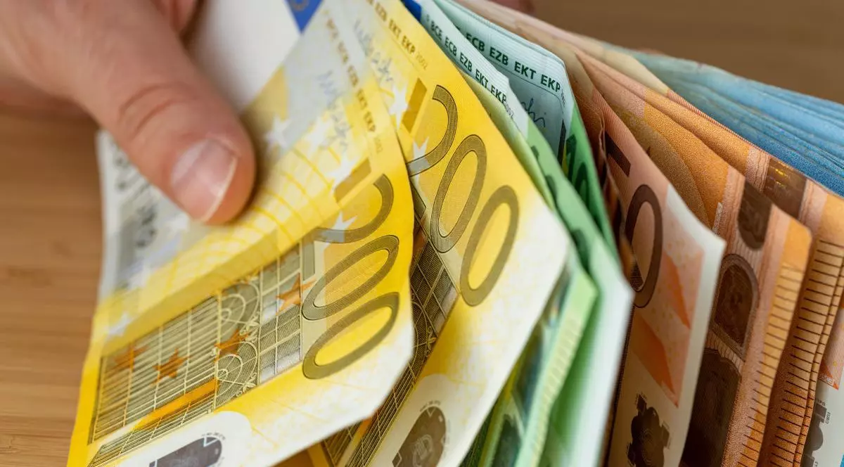 Mai multe bancnote de sute de euro sunt sprijinite pe o masă și ținute în mână de un bărbat