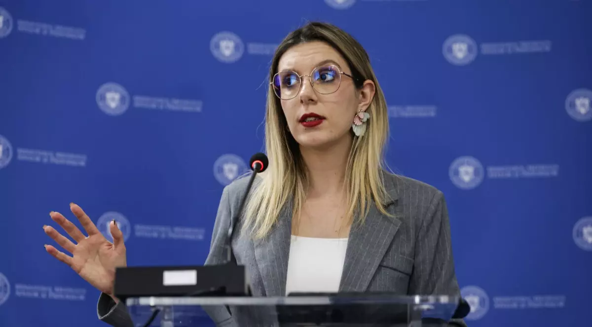 Diana Buzoianu într-un sacou gri și tricou alb în timp ce vorbește la microfon.