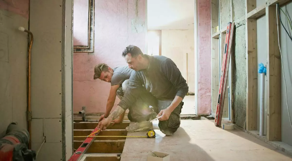 Muncitori reparând o casă, lucrează cu mistrie și cu materiale de construcție într-una dintre încăperi