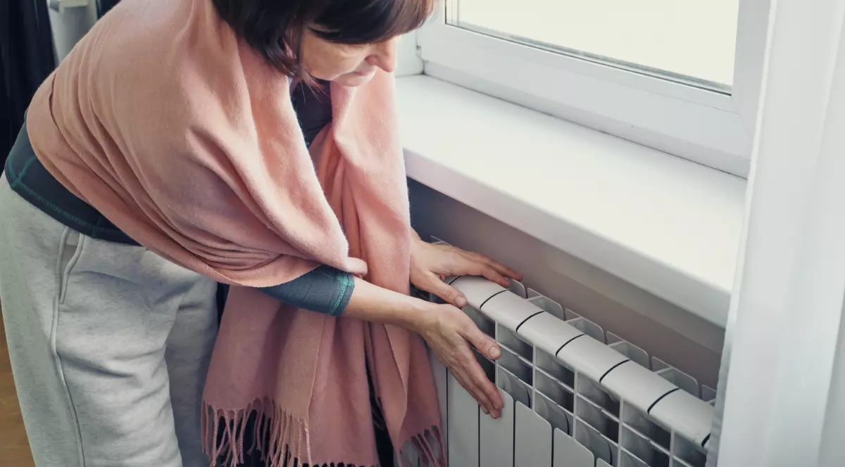 O femeie în vârstă cu părul roșu care pune mâna pe un calorifer să verifice dacă acesta este cald