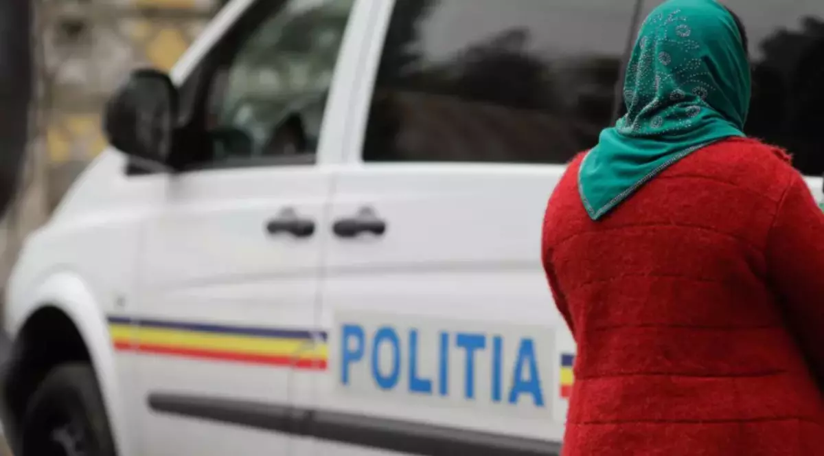 O femeie îmbrăcată în roșu, cu batic verde pe cap, lângă o mașină de poliție.