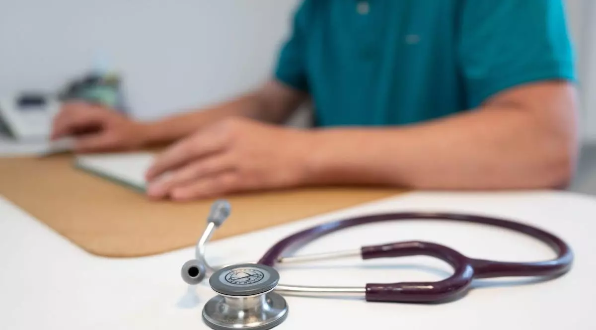 Un stetoscop stă pe un birou, lângă un doctor care consultă o fișă, 27 mai 2025
