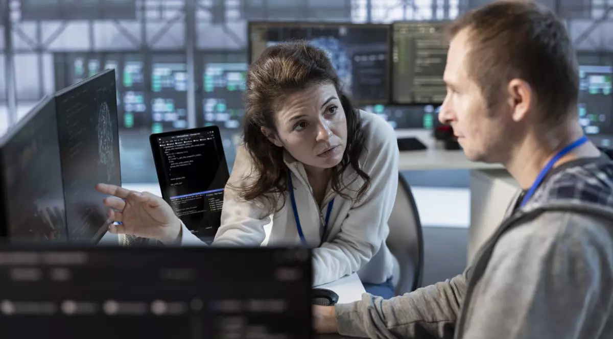 Un manager discută cu un angajat, care stă în fața unui calculator