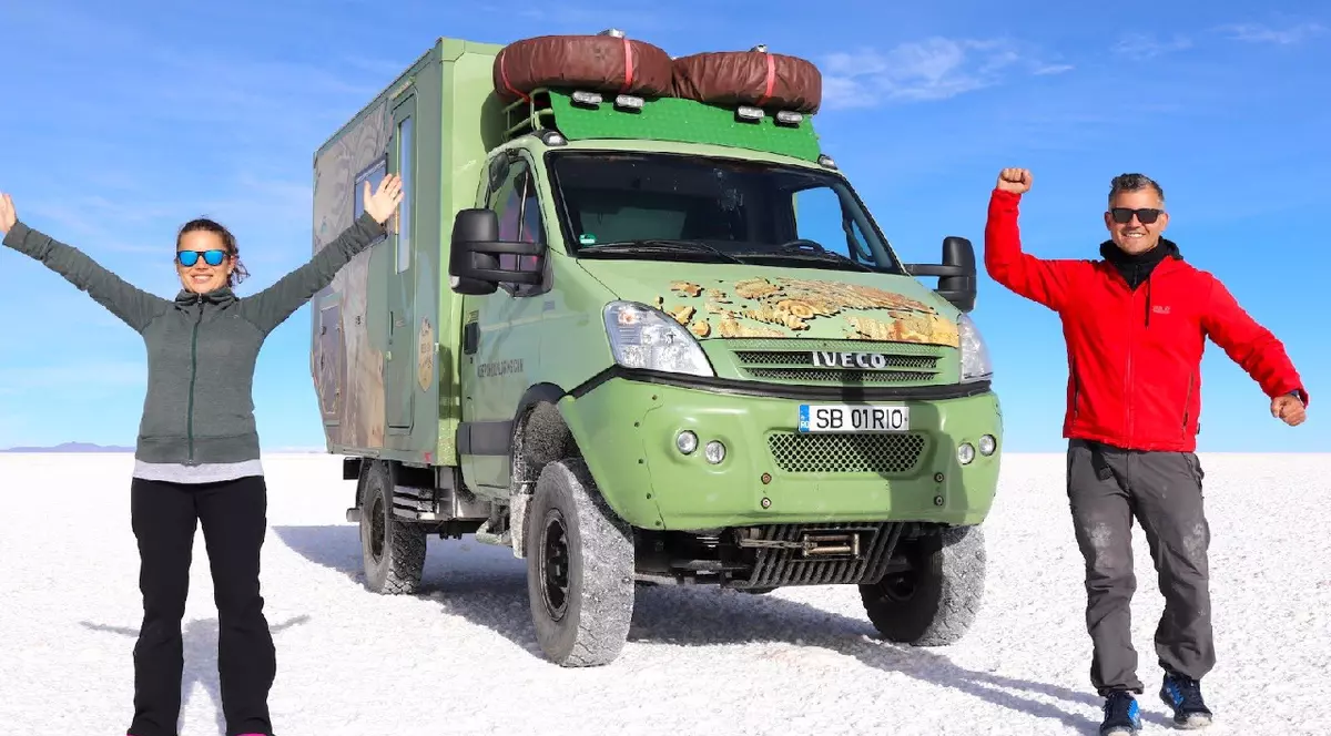 Un bărbat cu geaca roșie și o femeie cu geaca gri pozează lângă un camion verde