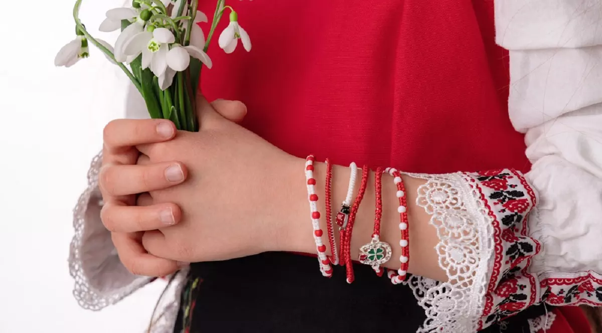 La ce mână se pune șnurul de mărțișor - o femeie, imbracata in port popular, tine in mana un buchet de ghiocei, iar pe mana stanga are mai multe snururi de Mărțișor