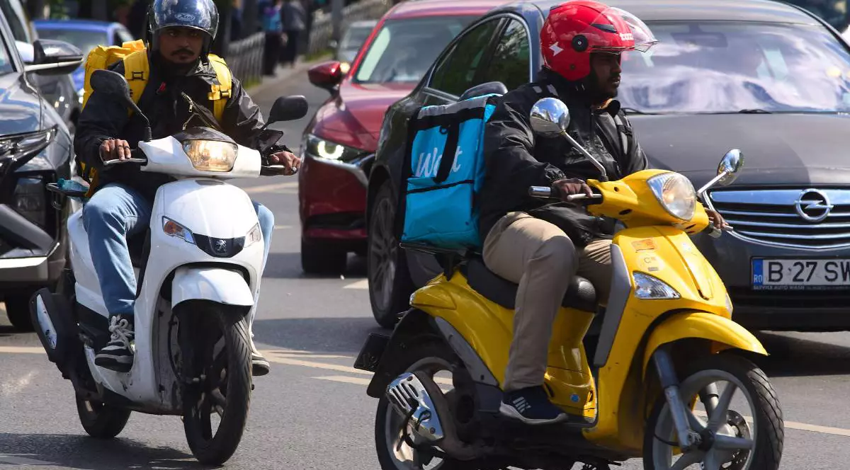 Curierii de livrare mâncare Glovo și Wolt, lucrători de origine străină, livrează mâncare în București, România.