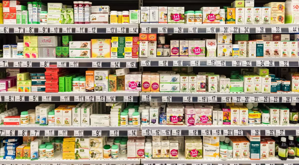 Medicamente pe rafturi, siropuri și alte produse într-o farmacie, cu prețurile afișate pe raft