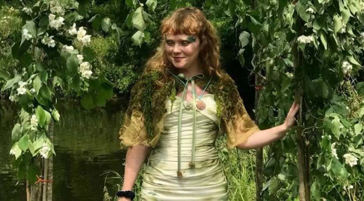 Tânăra Meg Avon, intr-un cadru de ceremonie, intre plante verzi, cu o roche vernil si o pelerina din muschi