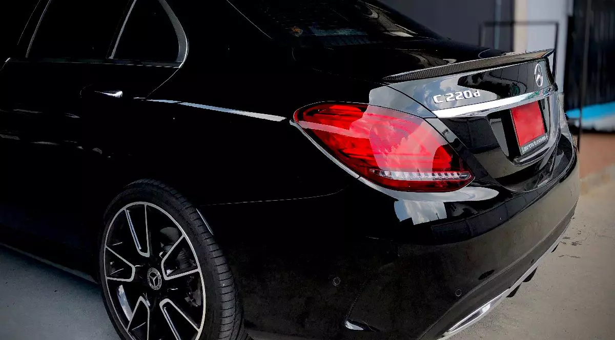 Fotografie cu o berlină Mercedes-Benz C220 neagră, elegantă, cu jante lustruite, parcată într-un garaj cu pereți de culoare închisă și un gard metalic în fundal.