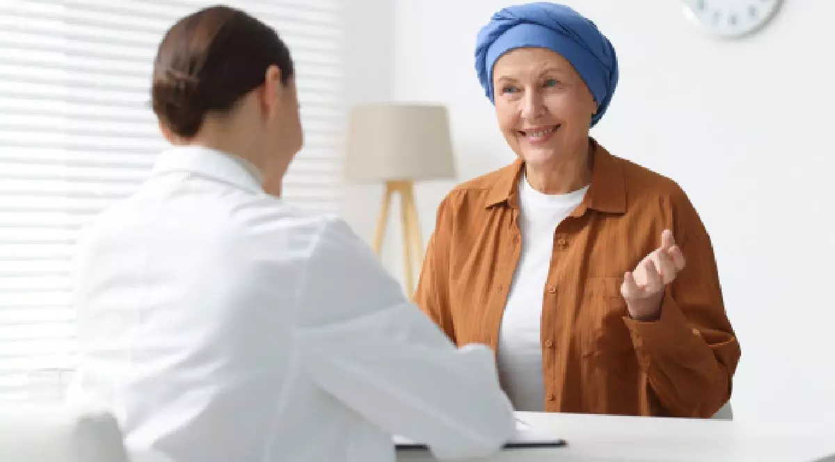 O femeie cu turban in cap sta in cabinetul medical si explica medicului. mielom multiplu. Traseul pacientului in Romania