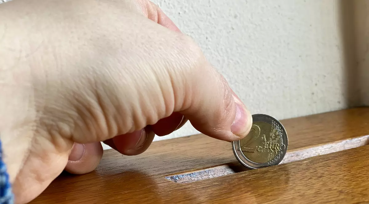 O persoană care pune o monedă de 2 euro într-o cutie maro din lemn.