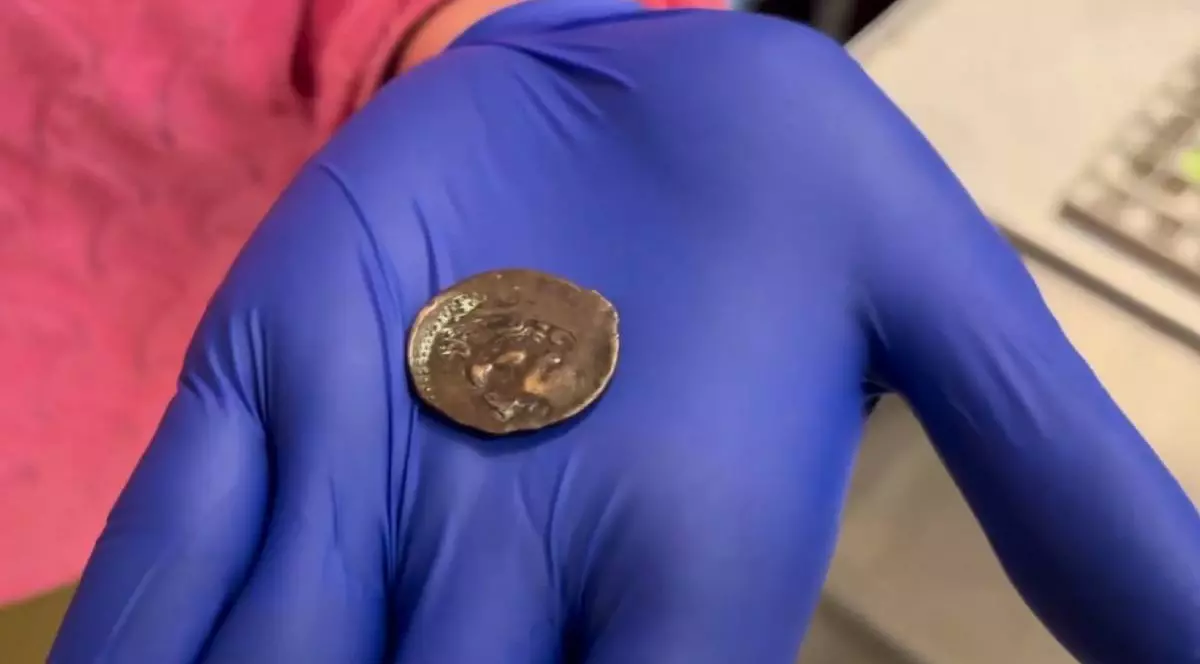 O moneda mica, de bronz, tocit[, veche de 2000 de ani, in palma unei persoane cu o manusa albastra