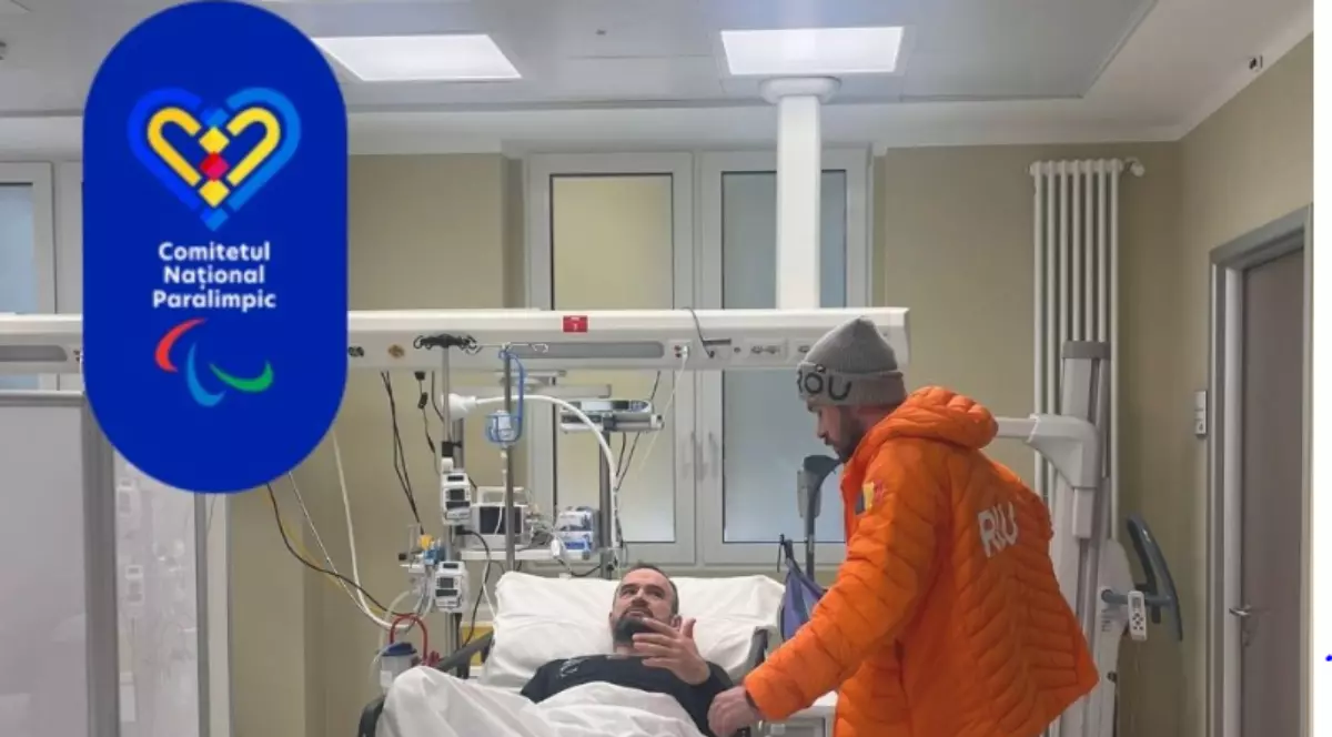 Un bărbat este întins pe un pat de spital, conectat la echipamente medicale, într-o sală de tratament. Lângă el se află o altă persoană îmbrăcată într-o geacă portocalie, care pare să discute cu pacientul, în timp ce în colțul imaginii apare logo-ul Comitetului Național Paralimpic.