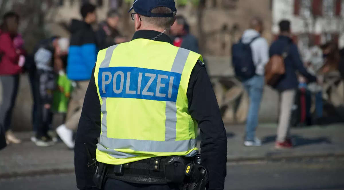 Un polițist care stă cu spatele și poartă o vestă pe care scrie POLIZEI