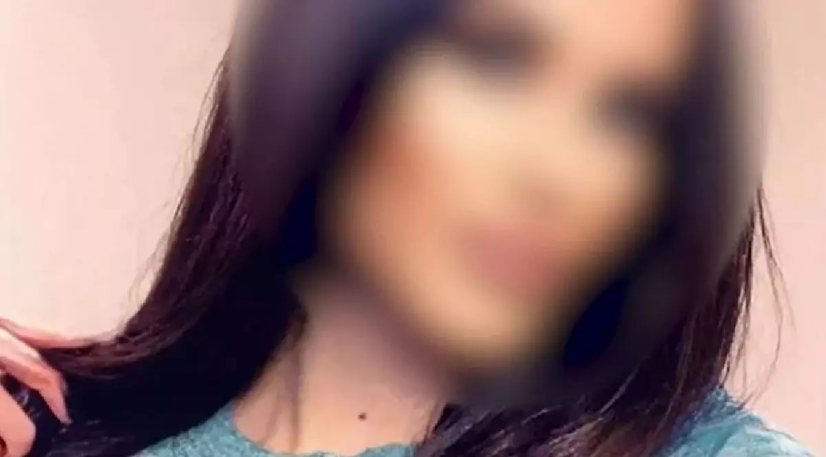 O fotografie neclară a unei femei cu părul lung și închis la culoare, îmbrăcată cu un top de culoare verde-albăstrui.