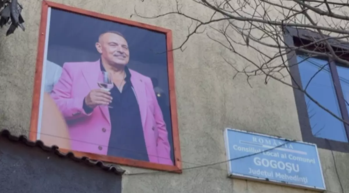 Un bărbat afișat pe un tablou pe fațada unei construcții. Acesta poartă un sacou roz și ține un pahar în mână.