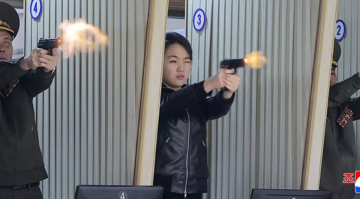 Kim Ju Ae, fiica lui Kim Jong Un, trage cu pisolul într-un poligon, având un ochi închis. Din țeava pistolului se vede ieșind o flacără, 12 martie 2026