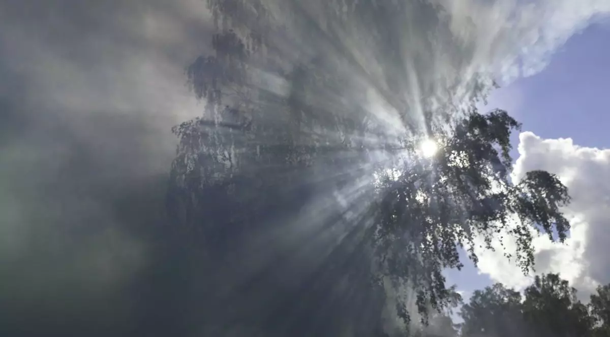 Cer albastru, nori și lumina soarelui în fundal, iar în stânga apar nori cu nuanțe vibrante de albastru