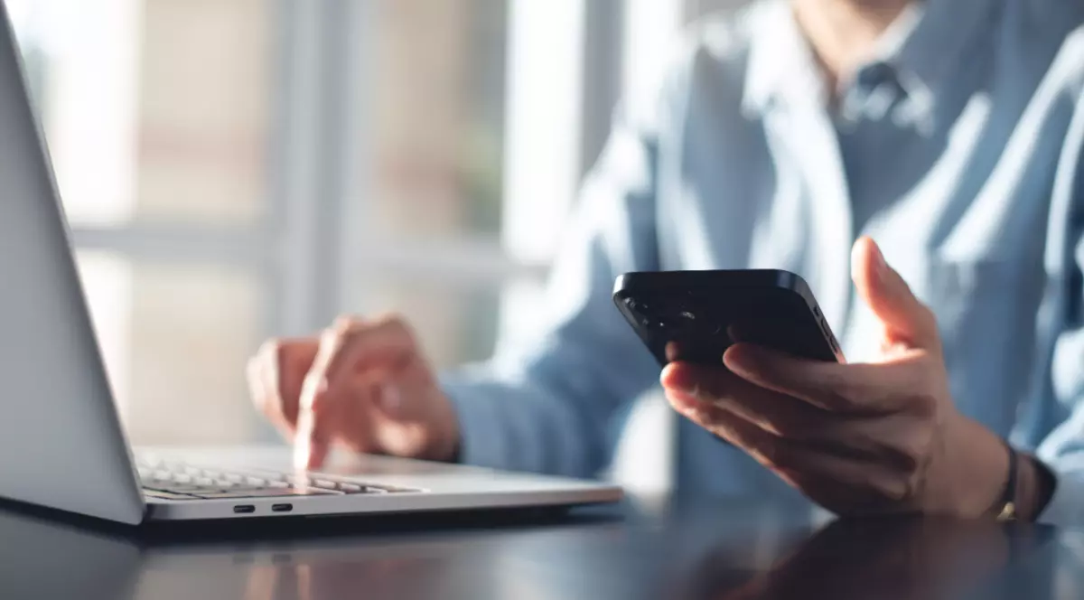 O femeie care se uită în ecranul laptopului și al telefonului mobil, după ce i-a venit factura