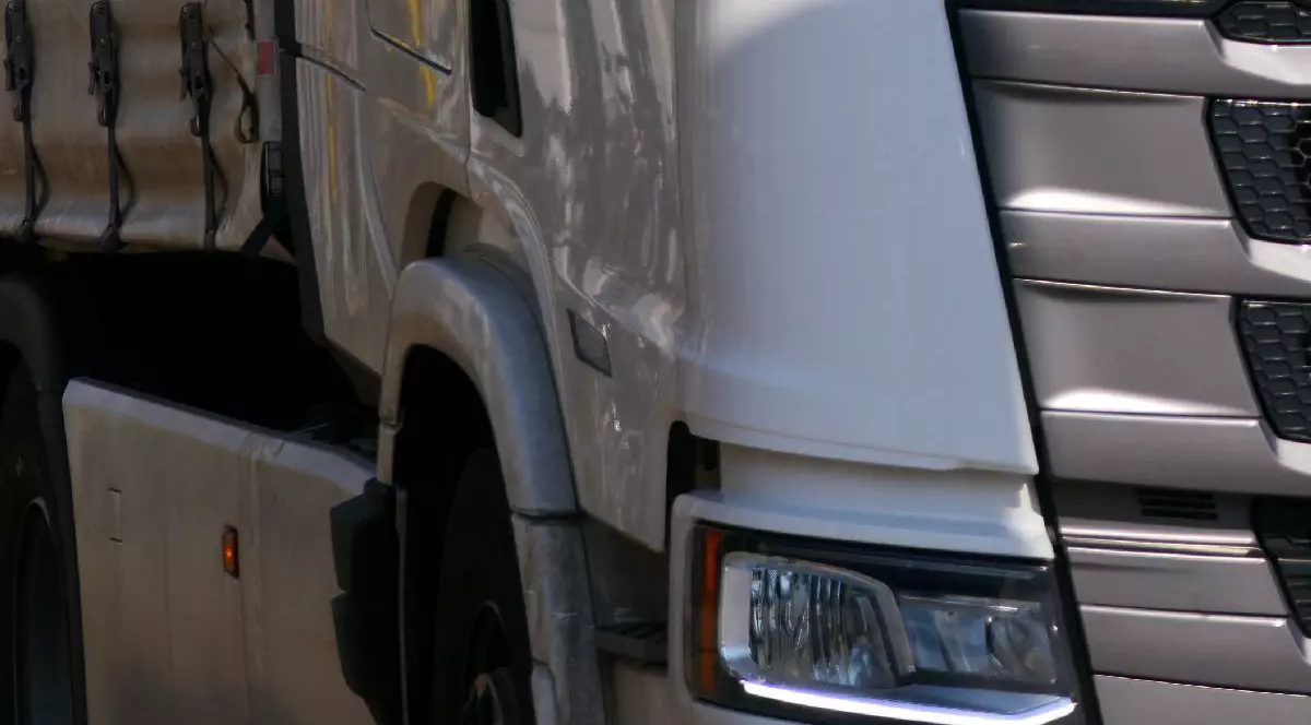 Fotografie în prim-plan a grilei frontale, a farurilor și a barei de protecție ale unui camion argintiu.