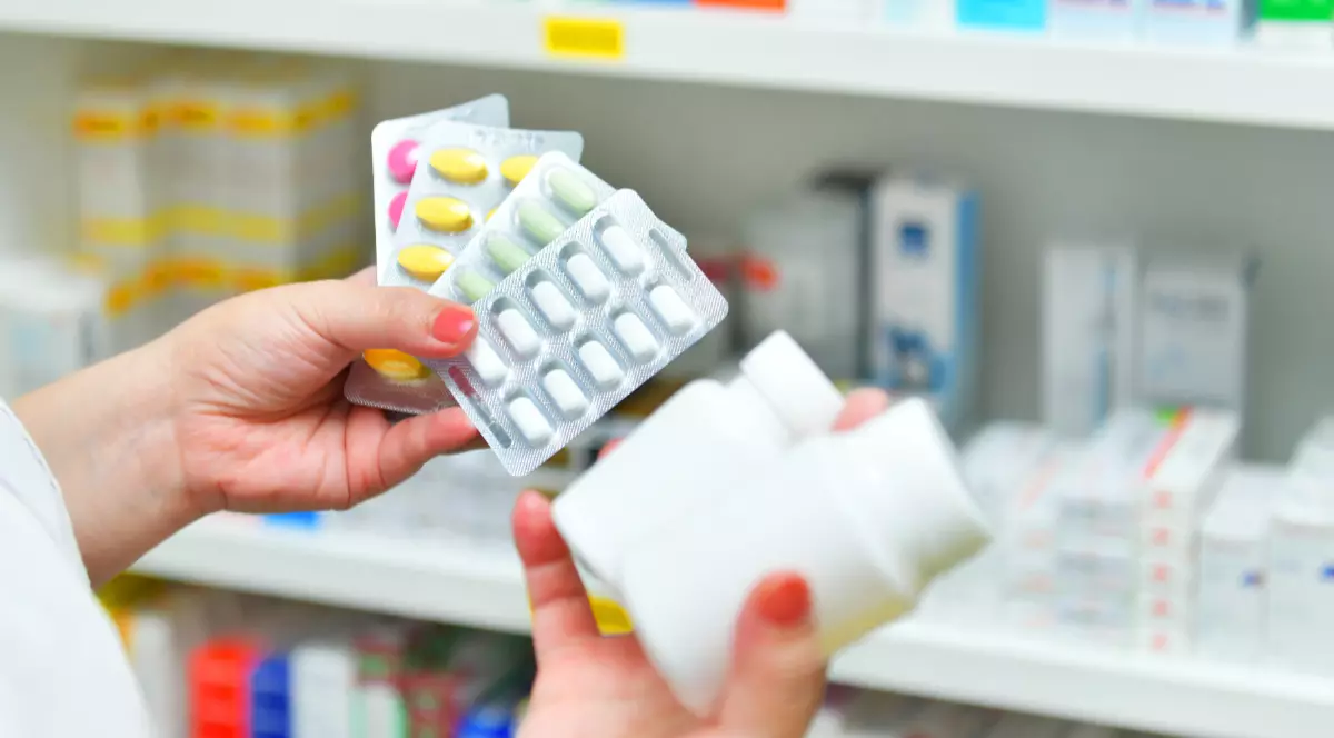O femeie care ține în mână mai multe flacoane și folii de medicamente, într-o farmacie