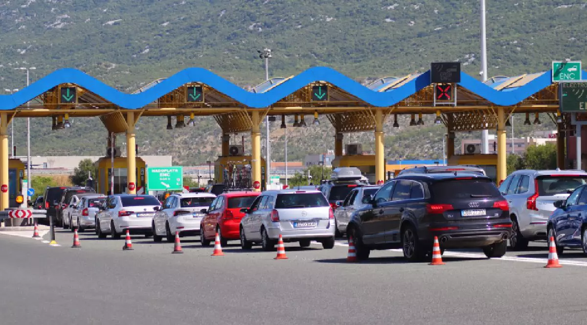 Fotografie cu un punct de trecere a frontierei aglomerat, cu mai multe mașini, inclusiv sedanuri și SUV-uri, așteptând la coadă sub o structură cu acoperiș albastru.