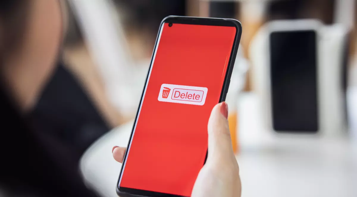 O femeie care ține un telefon în mână. Ecranul este roșu și scrie „Delete”