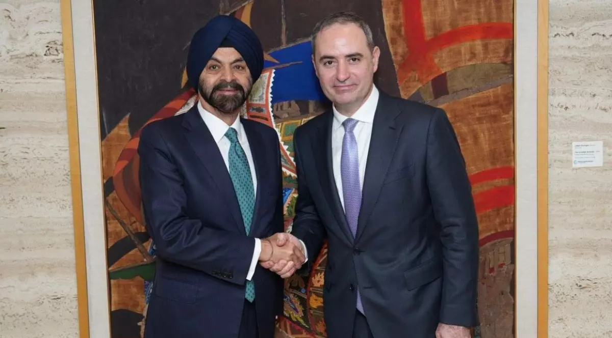 Imaginea surprinde doi oficiali îmbrăcați în costume, strângându-și mâna într-un gest formal, semn al unei întâlniri diplomatice sau al unui acord. Contextul și expresiile lor sugerează o colaborare sau un parteneriat între cele două părți.