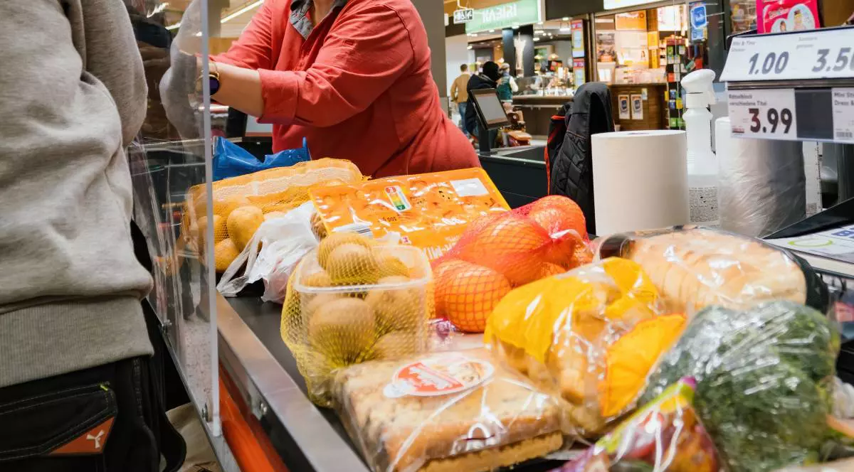 Alimente pe banda la casa, se vad fructe si legume, in spate o persoana casier in bluza rosie