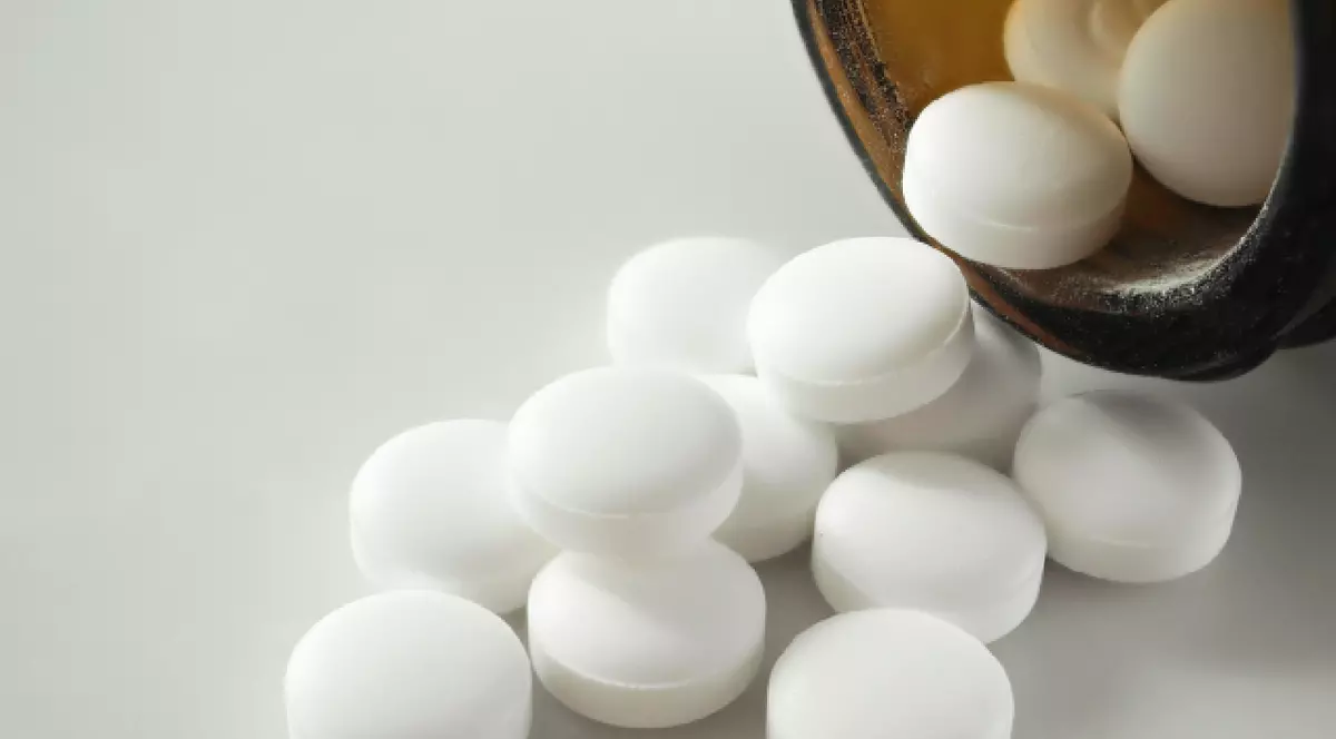 Pastilele albe se revarsă dintr-un flacon maro închis pe o suprafață gri deschis.
