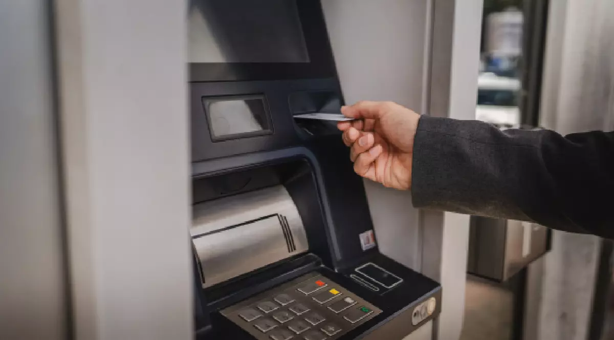 Prim-plan cu un bărbat care ține un card de credit în mână în timp ce folosește un bancomat pe stradă