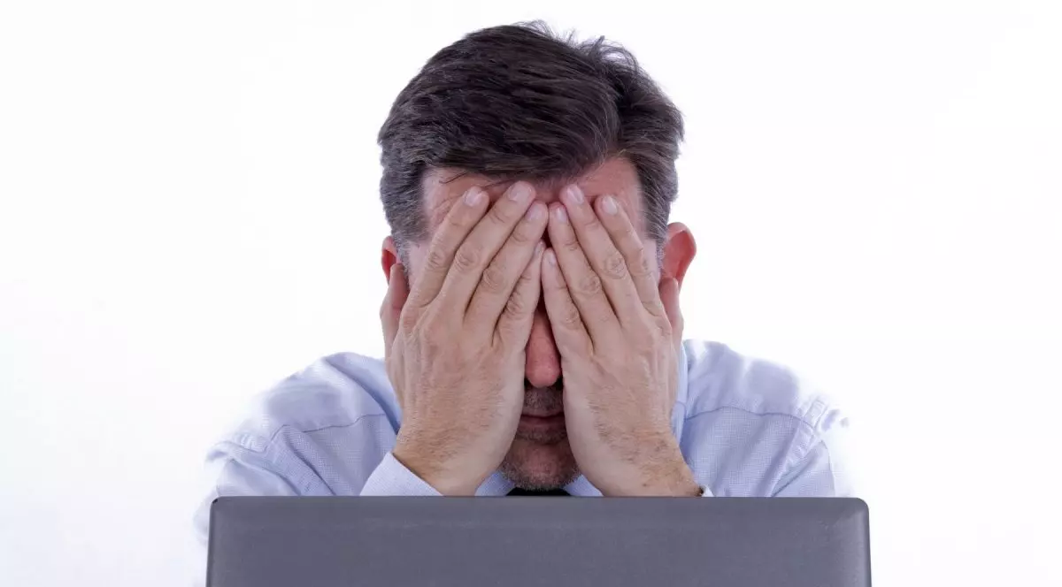 Un bărbat se ține cu mâinile de față înaintea unui laptop.