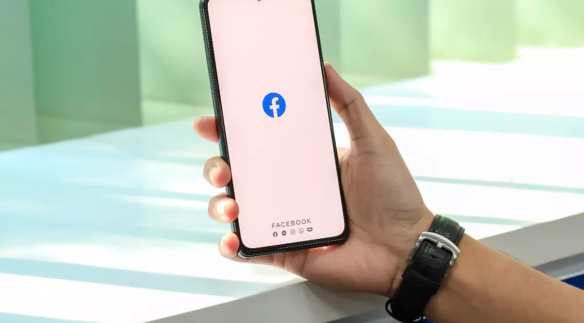 Un bărbat care ține un telefon în mână pe care accesează Facebook