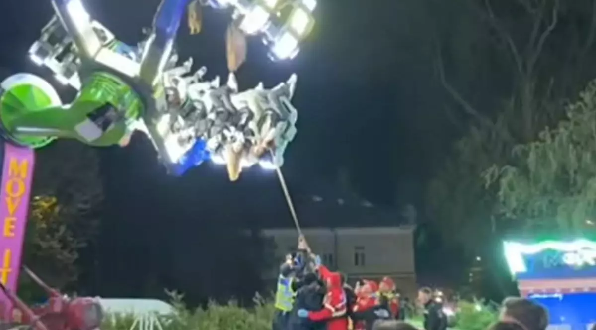 Captura video, imagini de noapte, copii blocati intr-un carusel luminos, sunt cu capul in jos, mai multi pompieri trag cu o sfoara de bratele caruselului