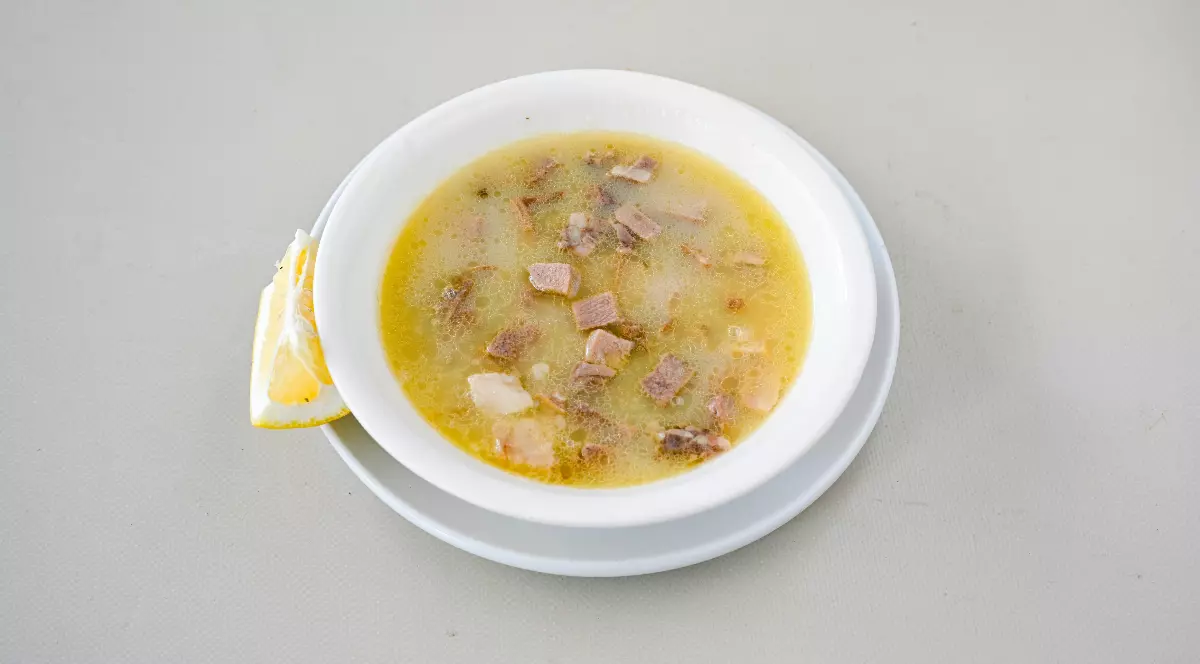 O porție de ciorbă de burtă este servită într-un bol alb, alături de o felie de lămâie. Preparatul are un aspect cremos, cu bucăți de carne vizibile, sugerând o rețetă tradițională consistentă.