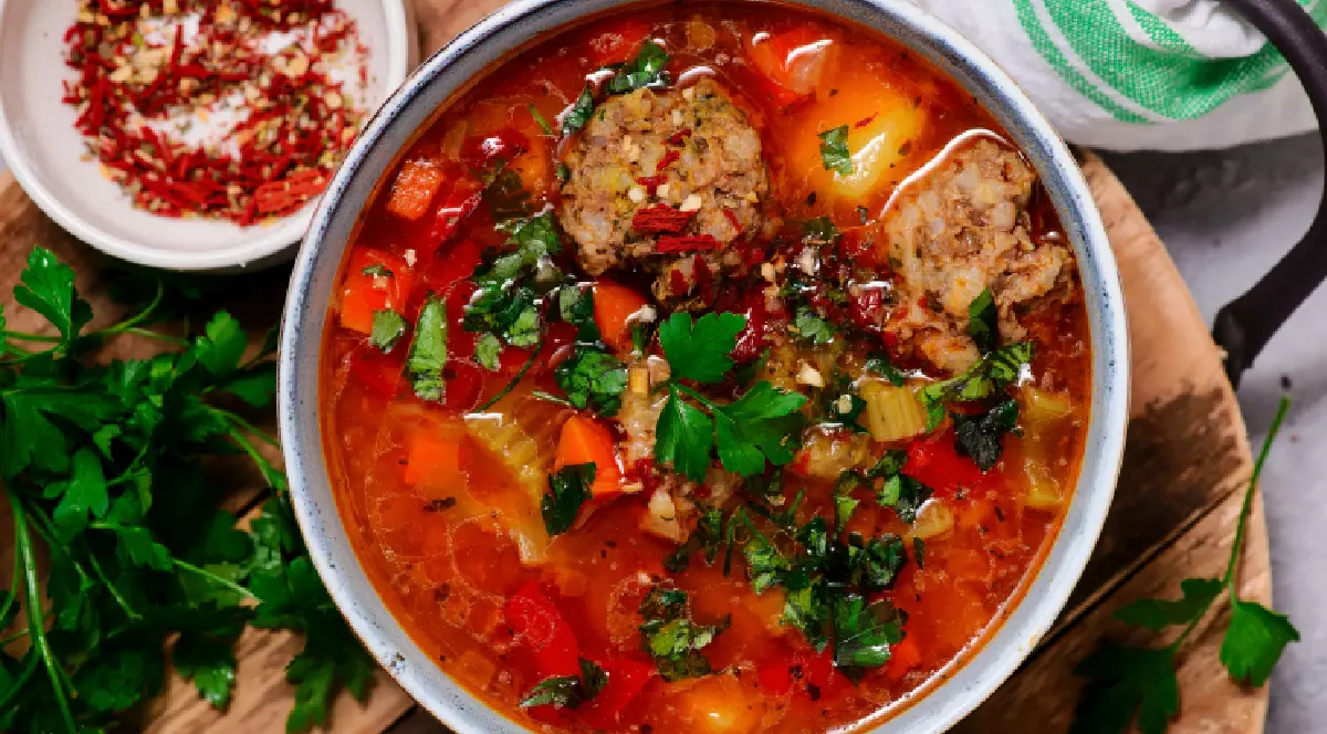 Pe o masă se află o farfurie cu ciorbă de perișoare