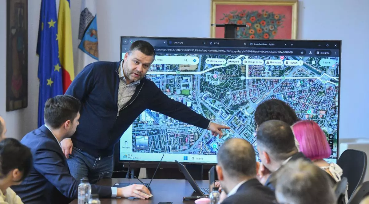 Ciprian Ciucu, primarul general al Capitalei, îmbrăcat cu blugi și pulover, arată cu mâna la un televizor pe care se vede o hartă, în timpul unei ședințe la Primăria București