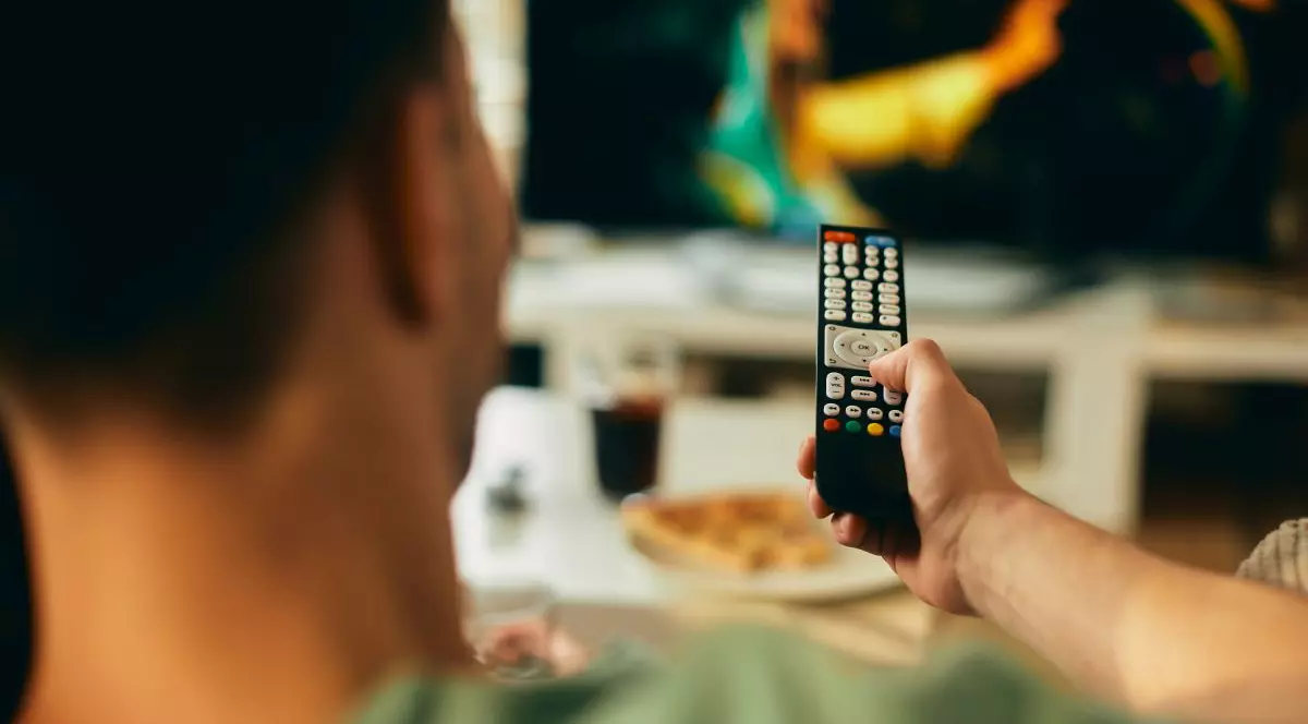 Close-up of man changing channels while watching TV at home.