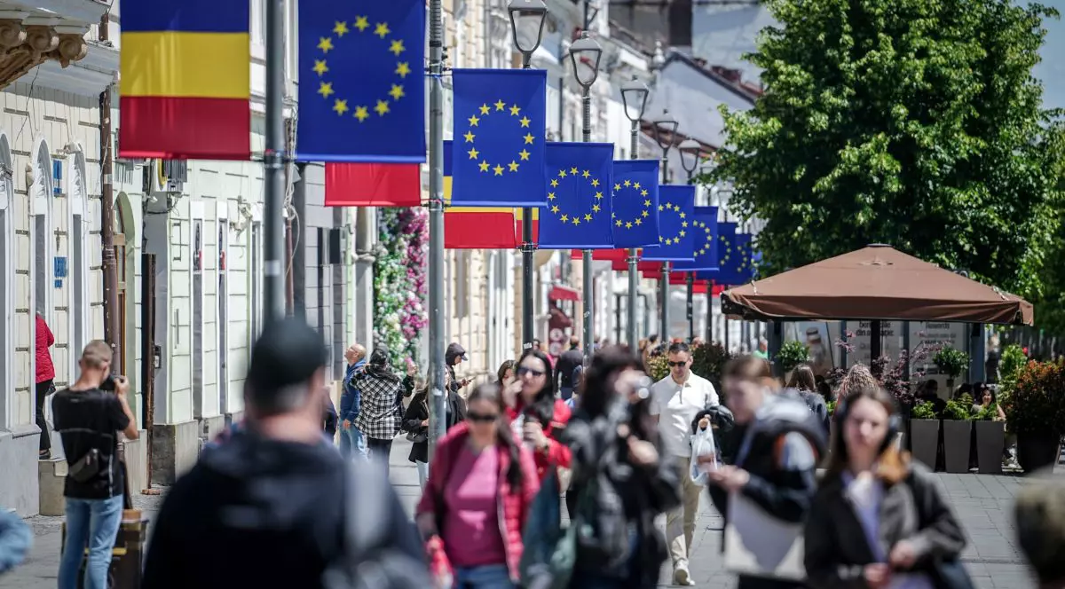 Fotografie de pe o stradă din Cluj, mai mulți oameni merg sub niște steaguri ale României și Uniunii Europene.