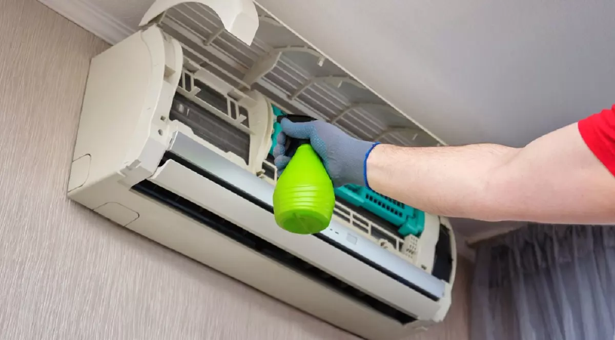 Curățarea aerului condiționat - UN barbat curăță unitatea interioară a aparatului de aer condiționat