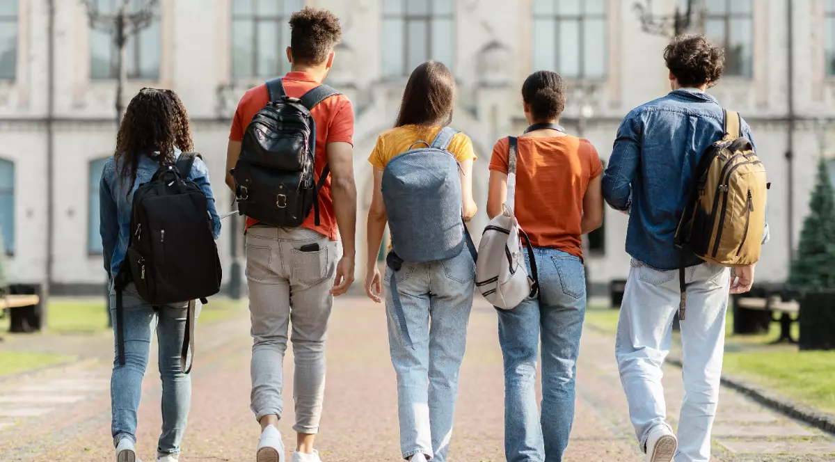 Un grup de cinci elevi de gimnaziu care merg pe alee cu ghiozdanele în spate